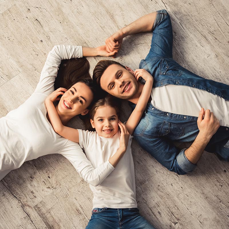 Top view of cute little girl and her beautiful young parents looking at camera and smiling while lying on the floor at home